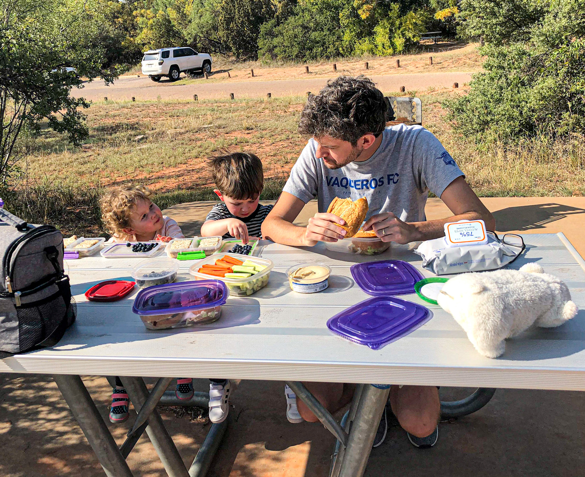 A dad and two toddlers have a healthy picnic during a road trip.
