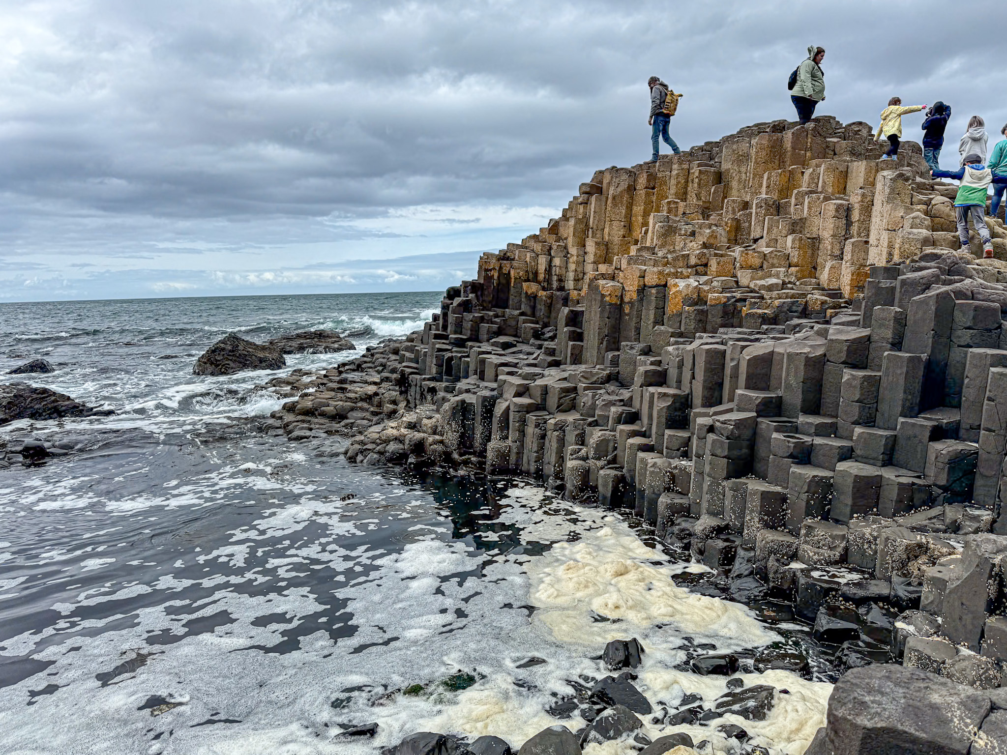 A view of the basalt columns in northern Ireland next to a rough sea with people climbing and exploring.