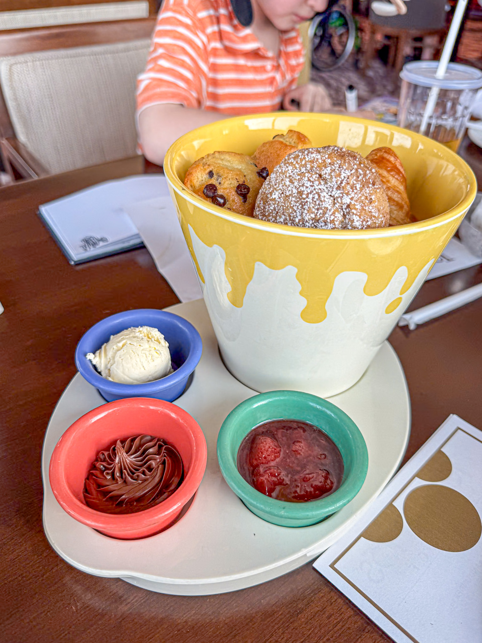 A paint bucket of pastries with side dishes of butter, strawberry jam and chocolate spread at Topolino Terrace at Disney World.
