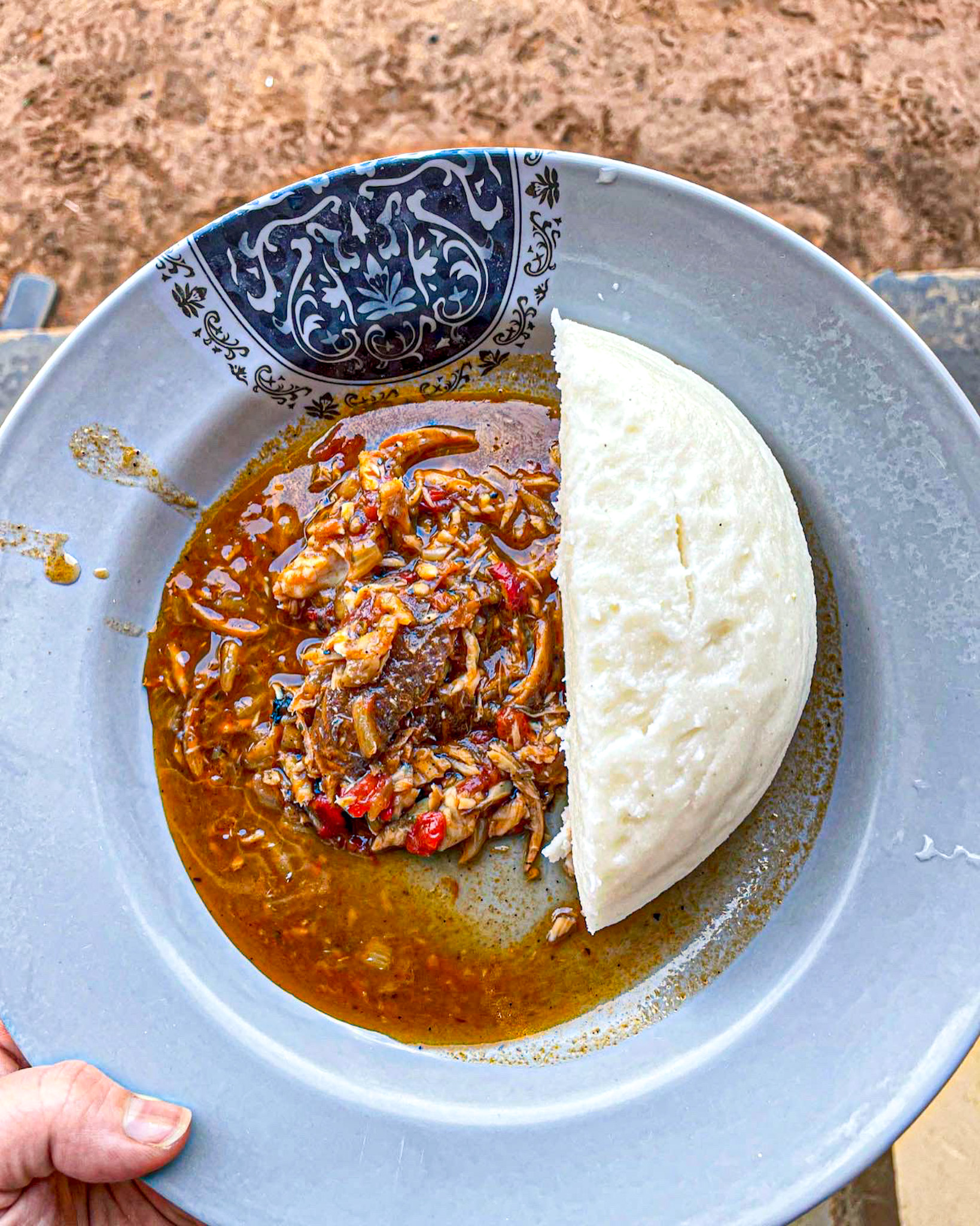 A plate of Ugandan food featuring a serving of posho (maize meal) and a rich stew made with shredded fish, vegetables, and spices in a reddish-brown sauce.