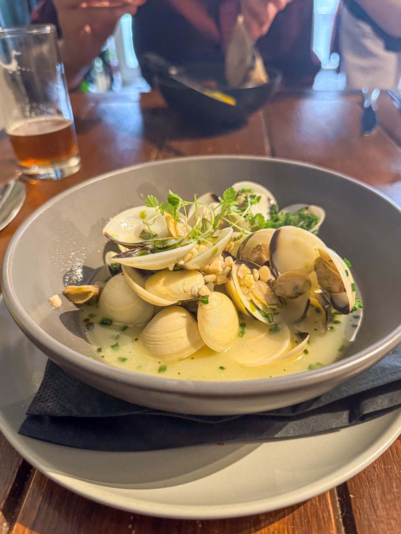 A bowl of clam soup garnished with herbs, served on a wooden table at a restaurant.