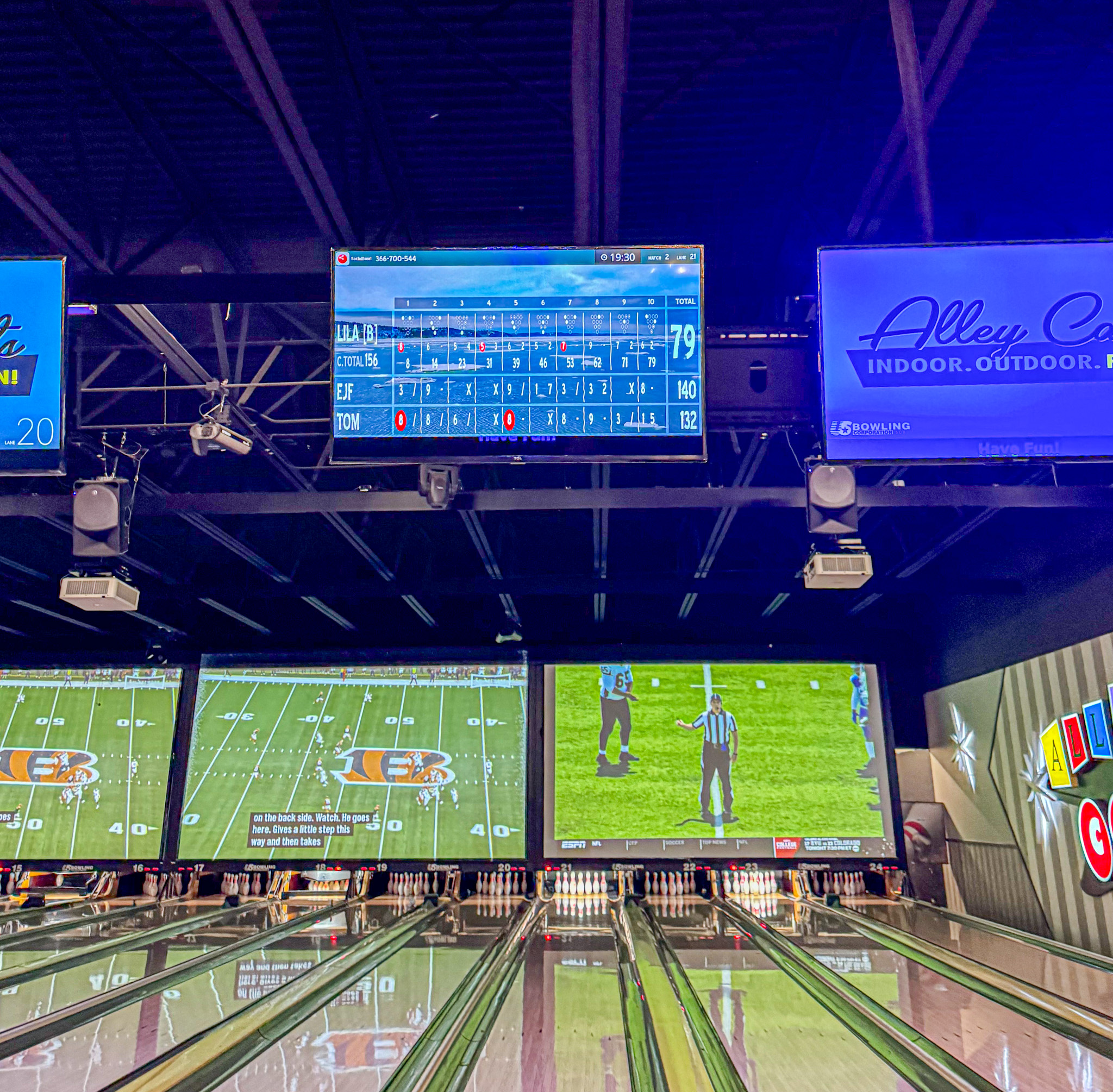 Alley Cates bowling alley in Arlington, Texas with electronic scoreboards and football games shown on large screens above the lanes.