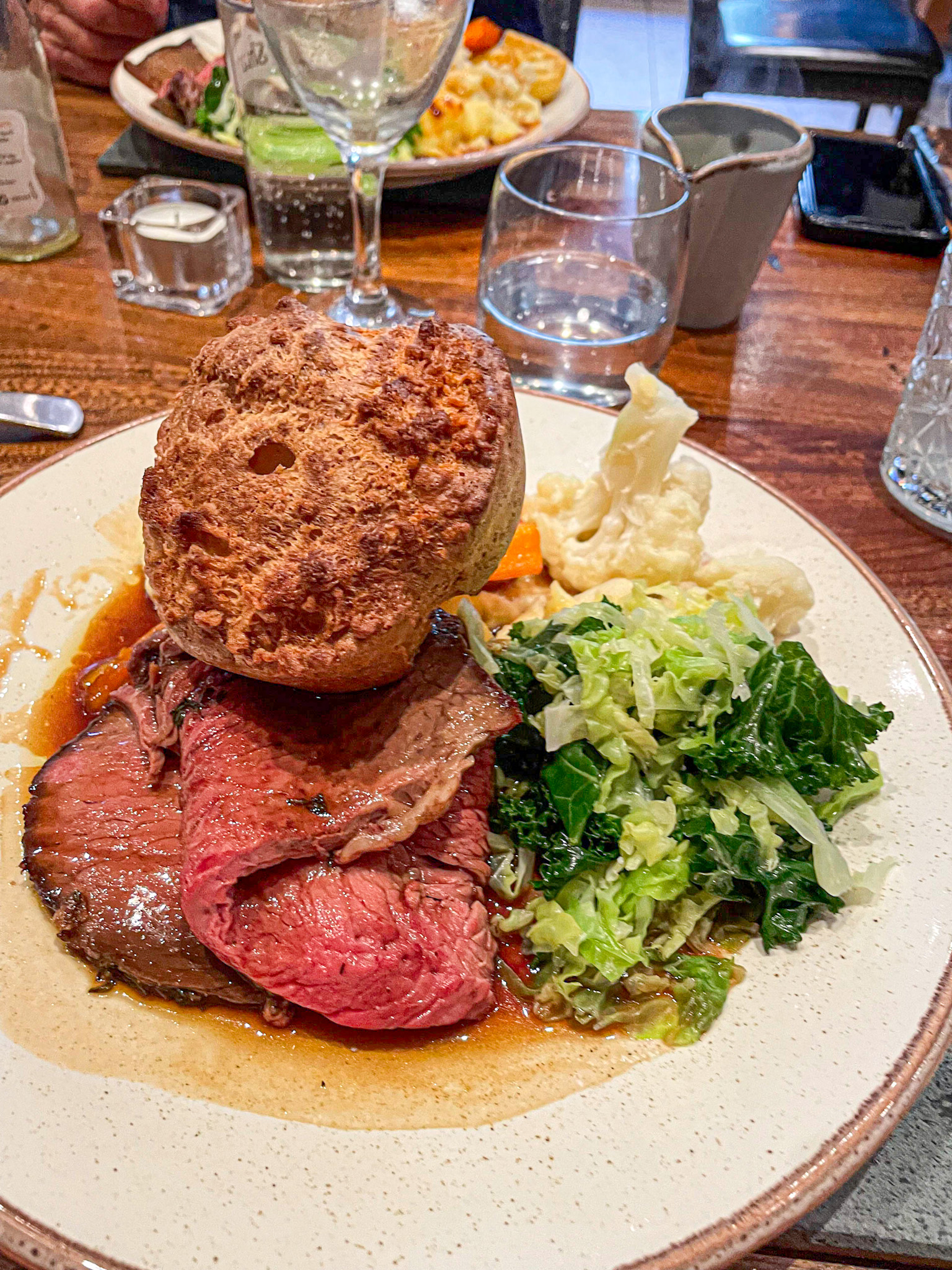 Plate of roast beef, Yorkshire pudding, green vegetables, and cauliflower on a wooden table in Platos restaurant in Kirkby Lonsdale.