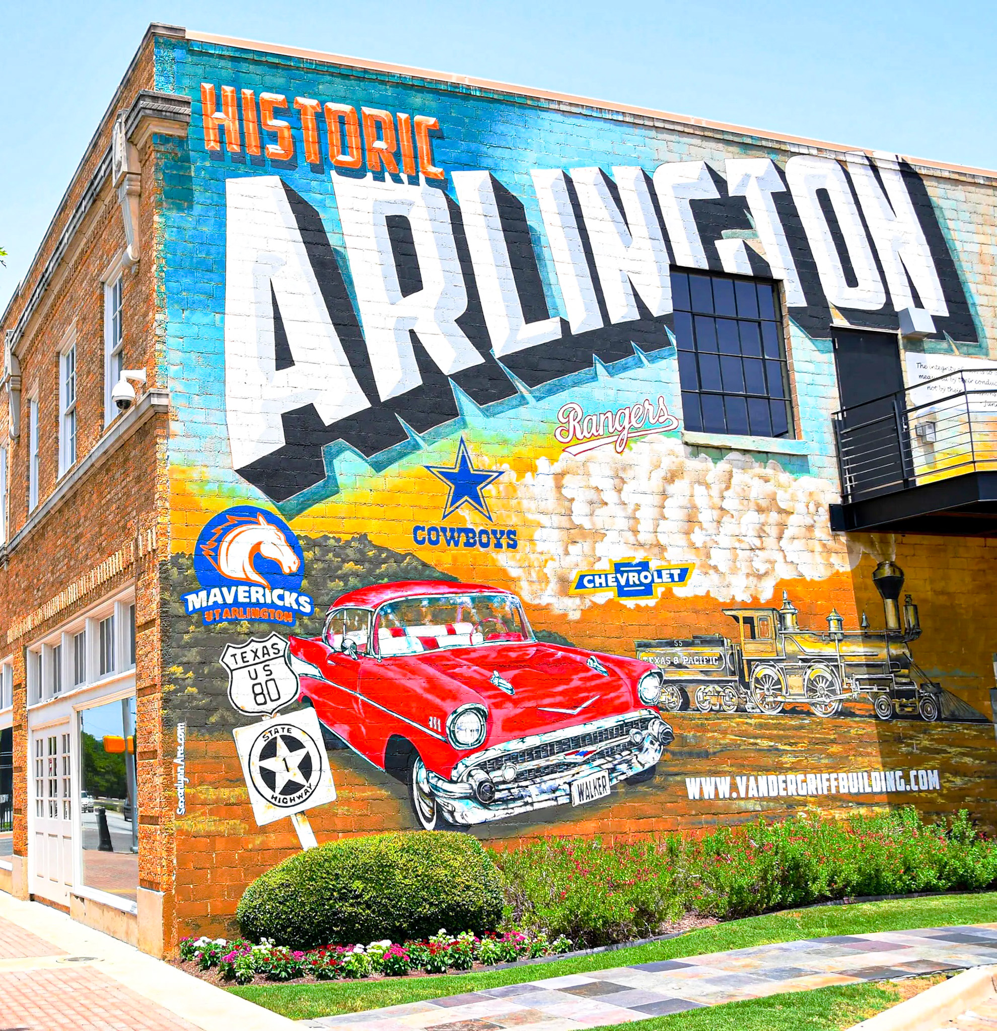 Colorful mural on a brick wall reads Historic Arlington with classic car, train, and local sports team logos.