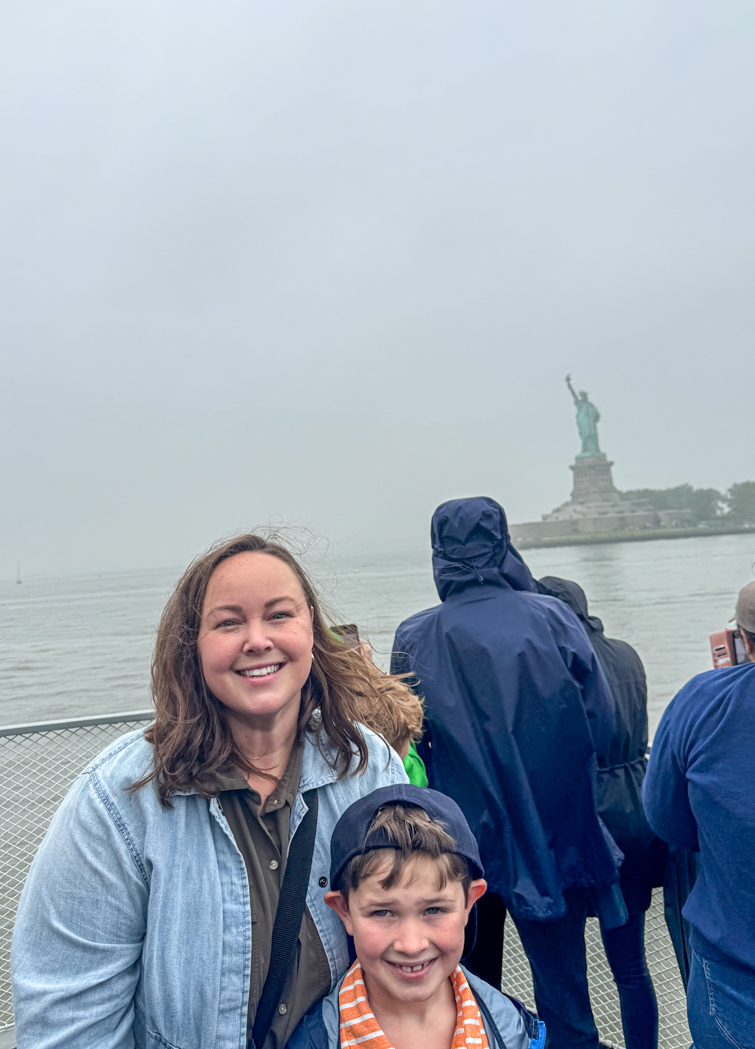 Smiling woman and boy on a boat, visiting the Statue of Liberty on a foggy day.
