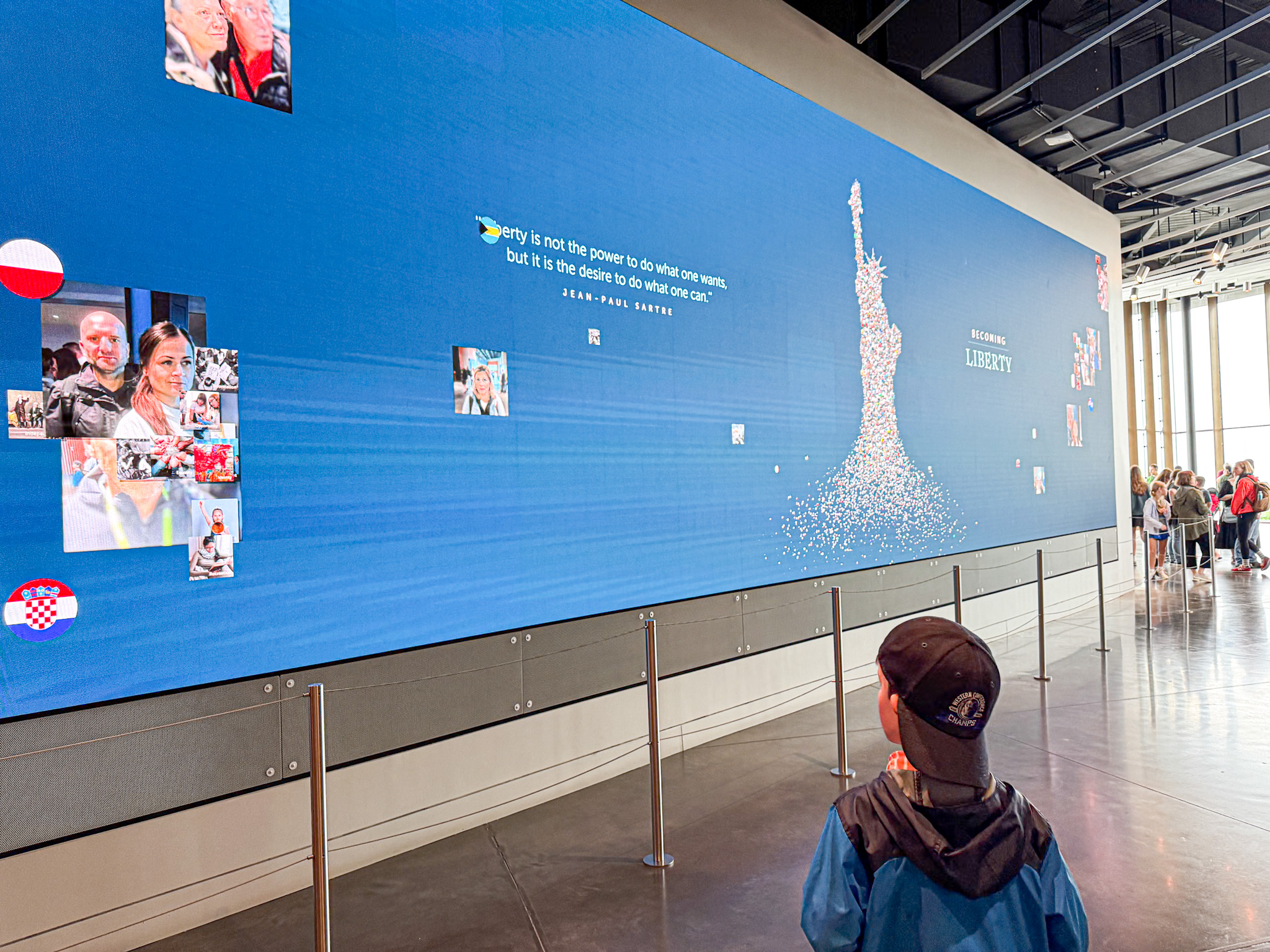 A child looks at a large digital screen displaying the Statue of Liberty and photos inside a modern exhibit.