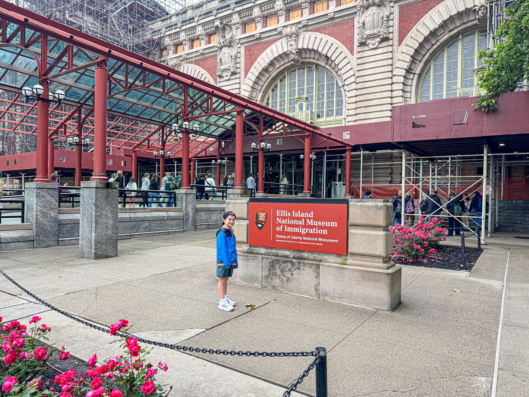A child stands near the Ellis Island National Museum of Immigration sign, with the building in the background.