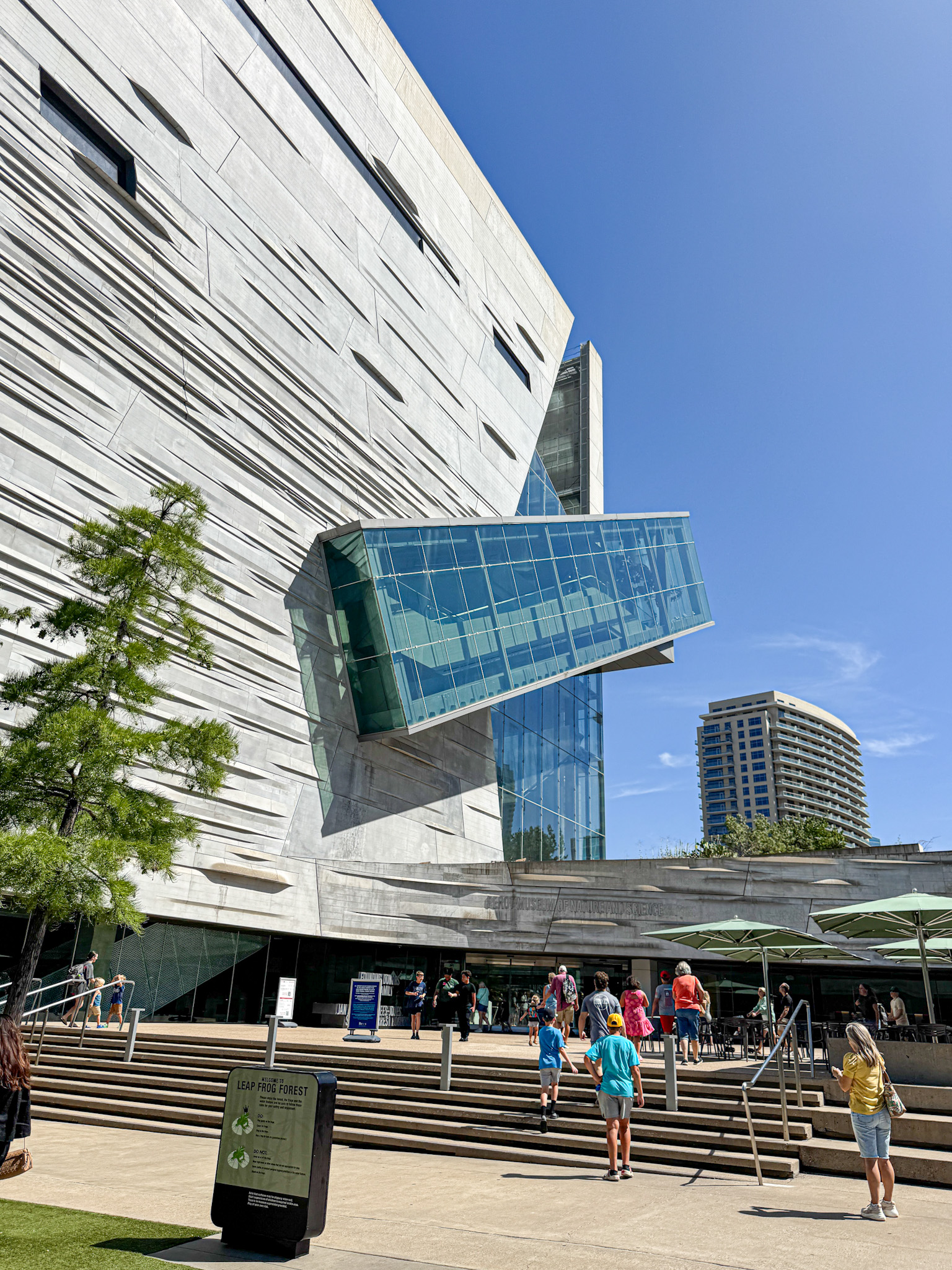 People stand outside the Perot Museum of Nature and History in Dallas, Texas with angular lines and a large glass projection on a sunny day.