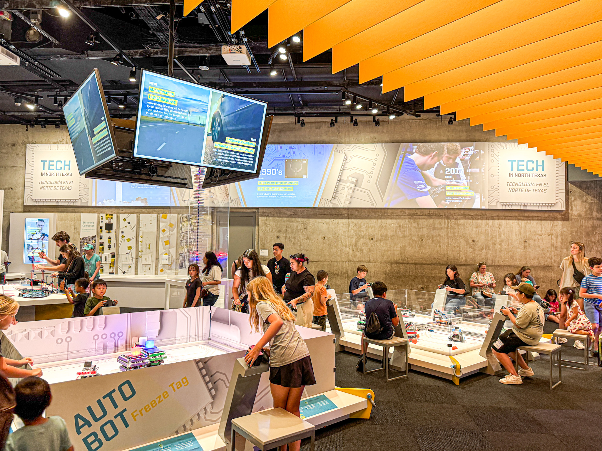 Children and adults interact with hands-on tech exhibits in a busy Texas Instruments Engineering and Innovation Hall at the Perot Museum. 