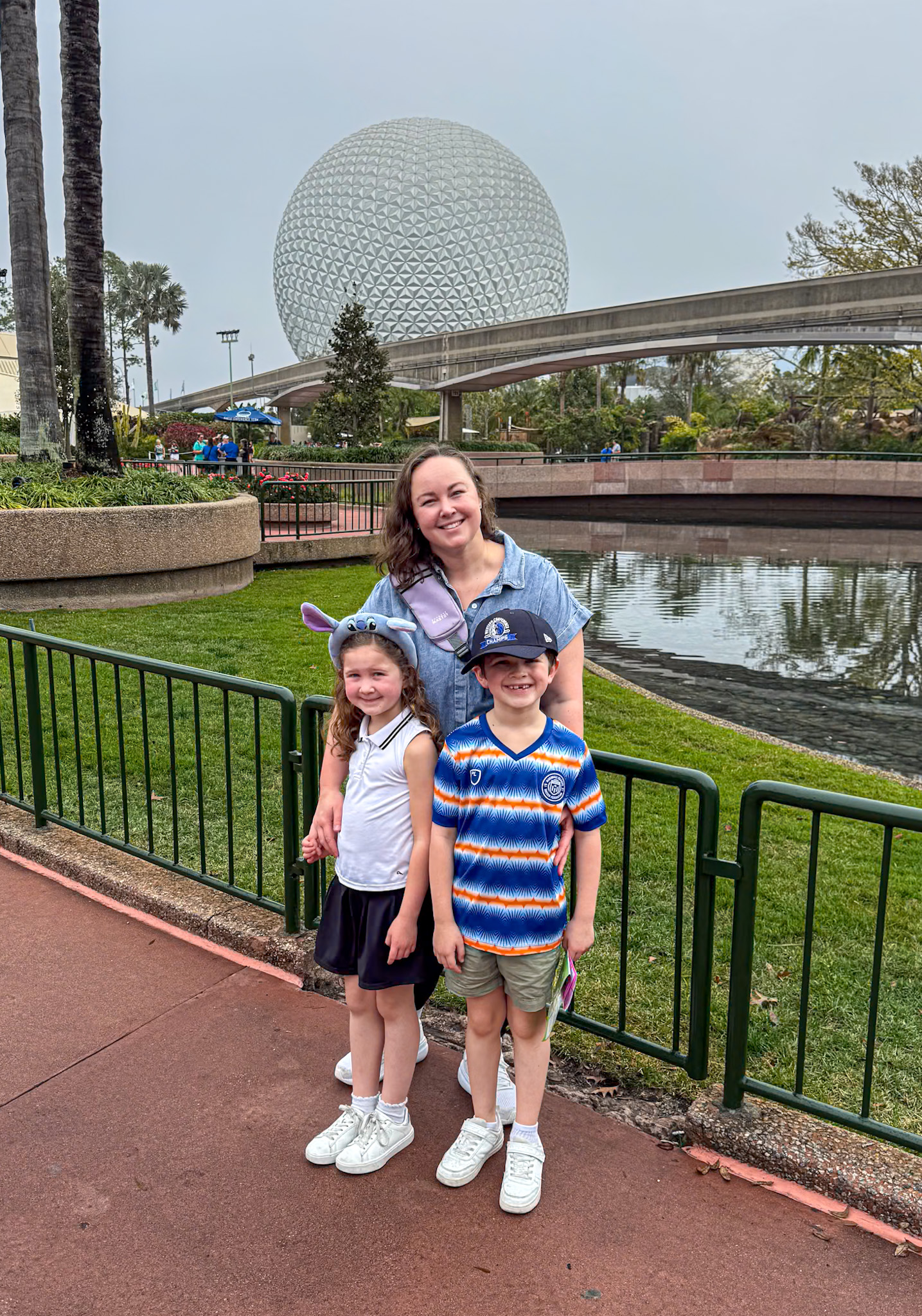 A woman and two smiling children pose in front of Epcot’s Spaceship Earth at Disney World.