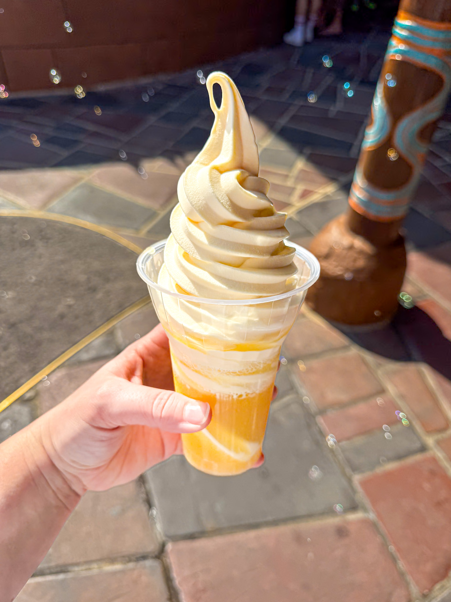 A hand holds a dole whip in a clear, outdoors on a sunny day in Magic Kingdom at Disney World.