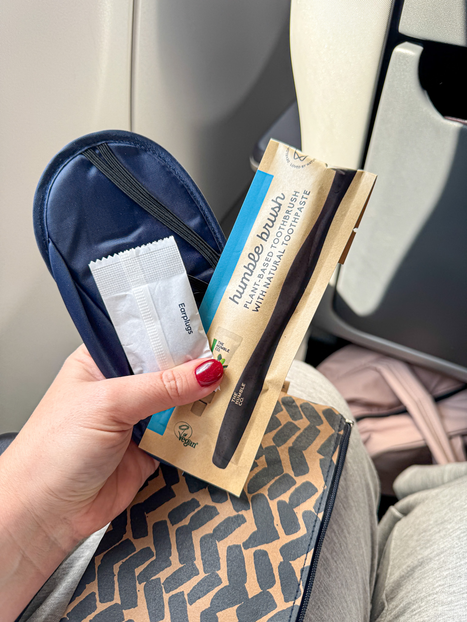 A hand holds a the contents of a Finnair Premium Economy amenity kit, with a toothbrush kit, earplugs and an eye mask.