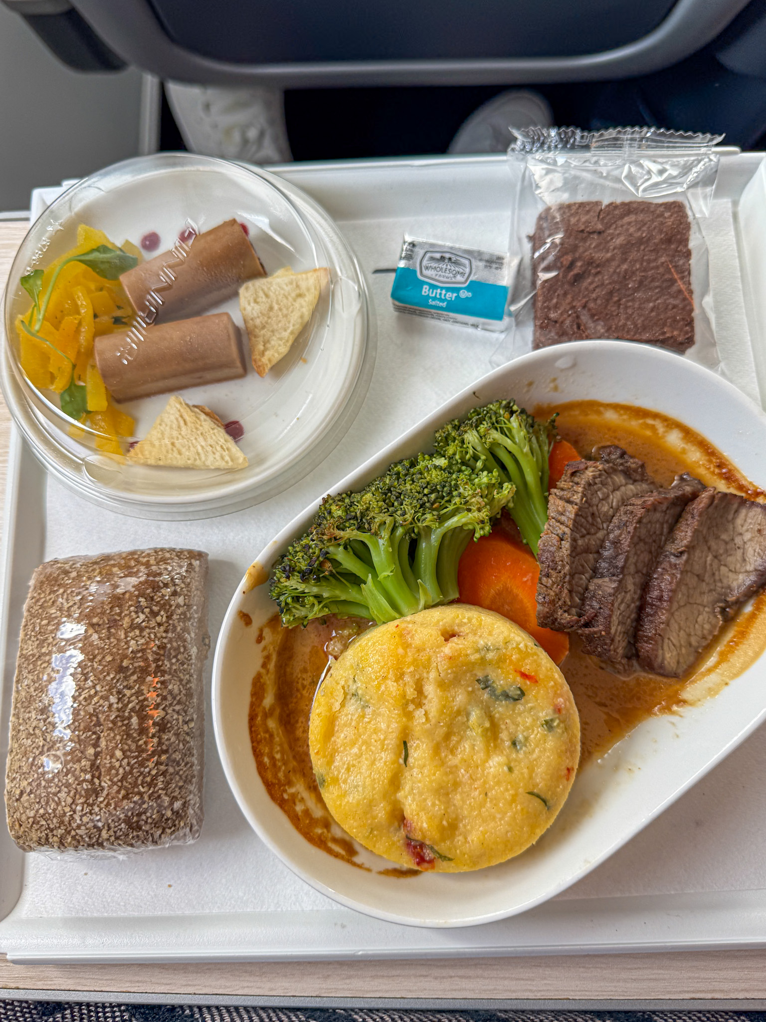 Finnair Premium Economy meal tray with beef, broccoli, carrots, cornbread, bread roll, salad, brownie, and butter.