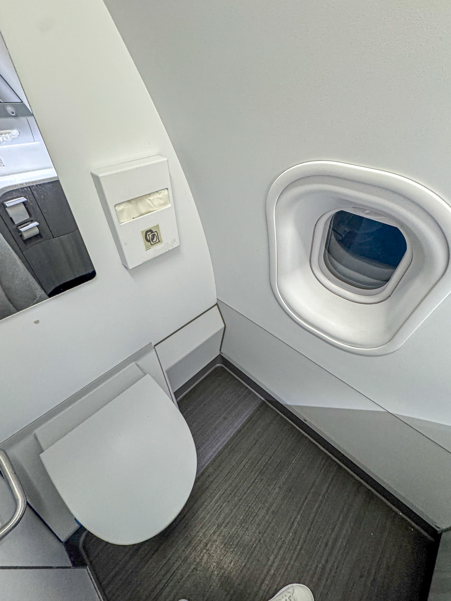 Airplane lavatory on Finnair with a toilet, tissue dispenser, and small window beside a gray floor.