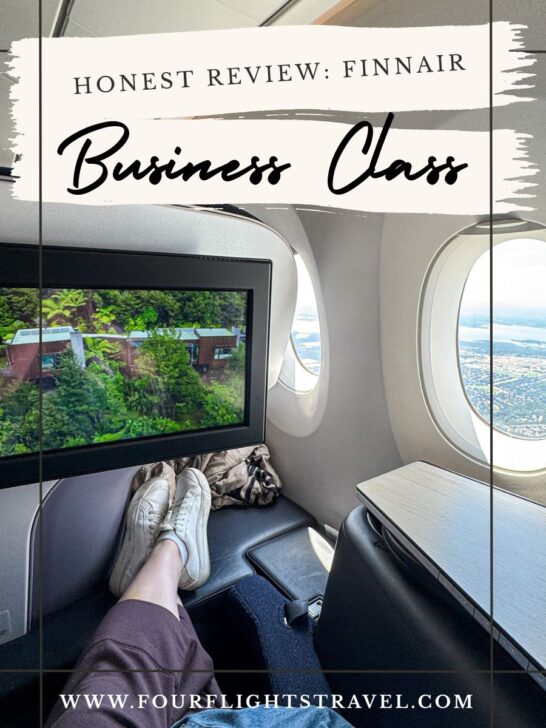 Person relaxing in Finnair business class seat, watching TV, with window view of sky and landscape.
