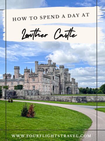 Large stone castle with towers and arches, surrounded by green lawns under a partly cloudy sky.