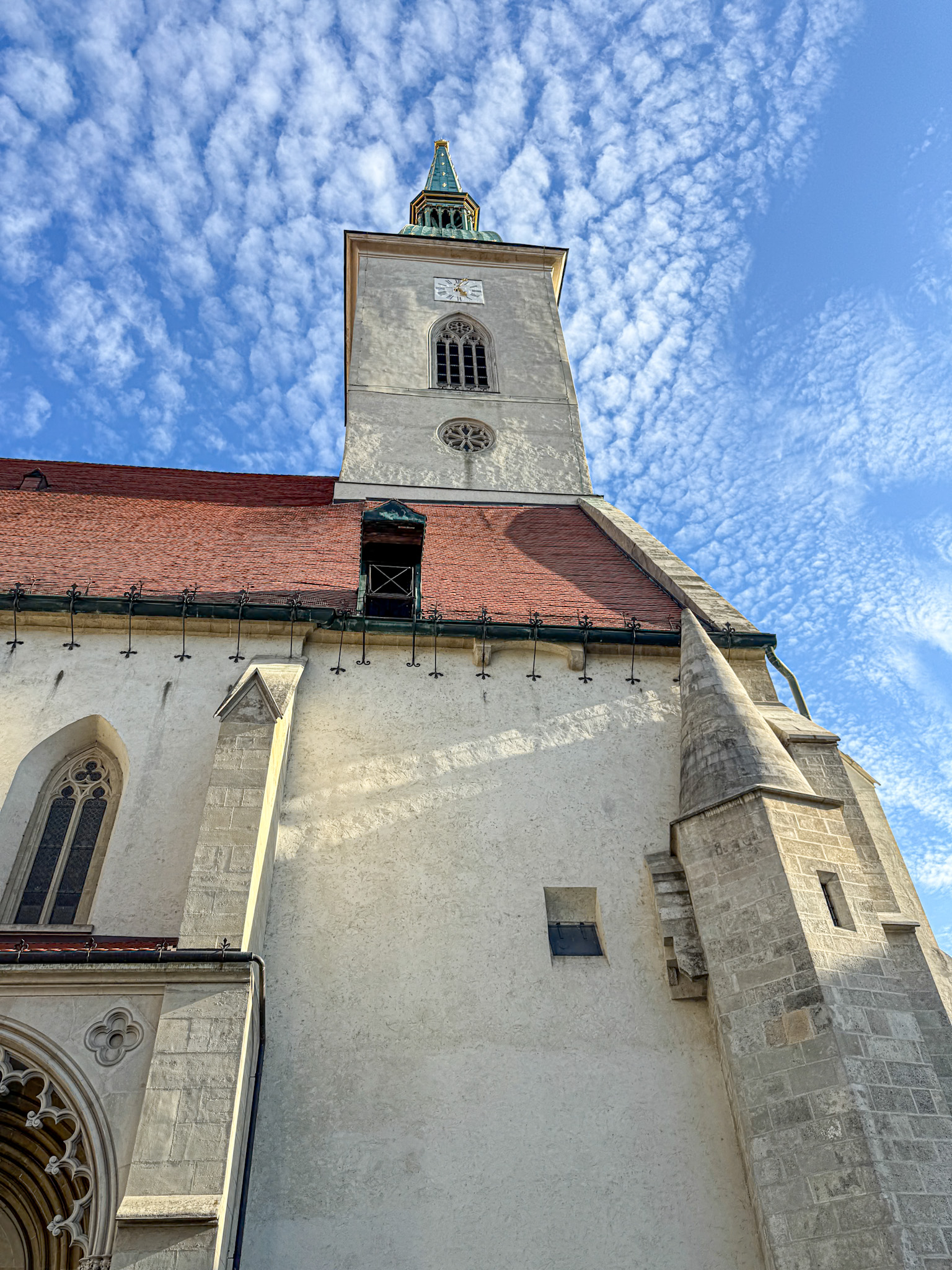St. Martin's cathedral in Bratislava, Slovakia with a clock tower and a red roof, set against a blue sky with scattered clouds.