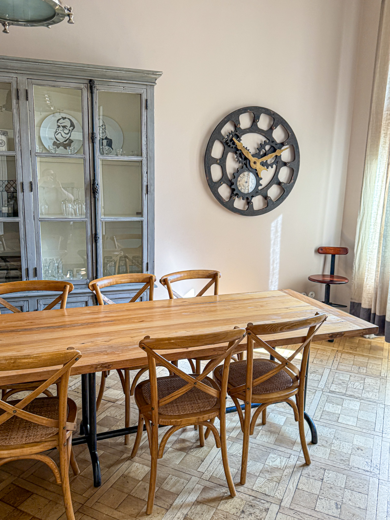 Dining room with wooden table, six chairs, glass cabinet, and a large wall clock above parquet flooring at the Malostranská Residence. 