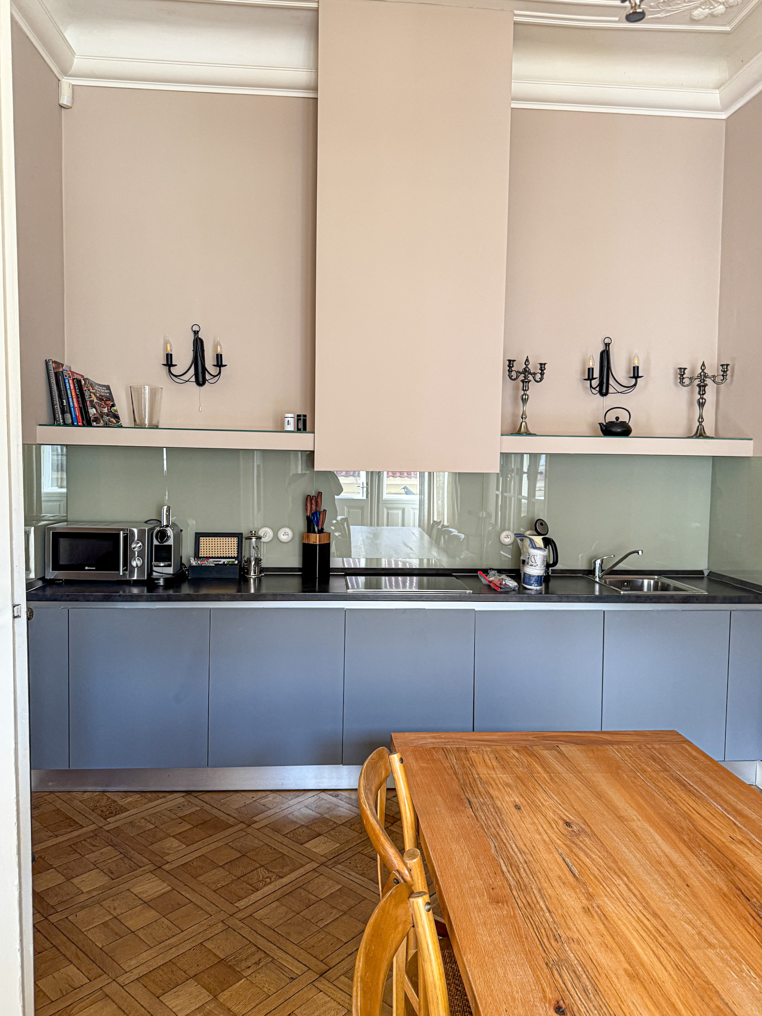 Modern kitchen with blue cabinets, wood table, wall sconces, and countertop appliances against a pale wall at a rental property in Prague, Czech Republic.