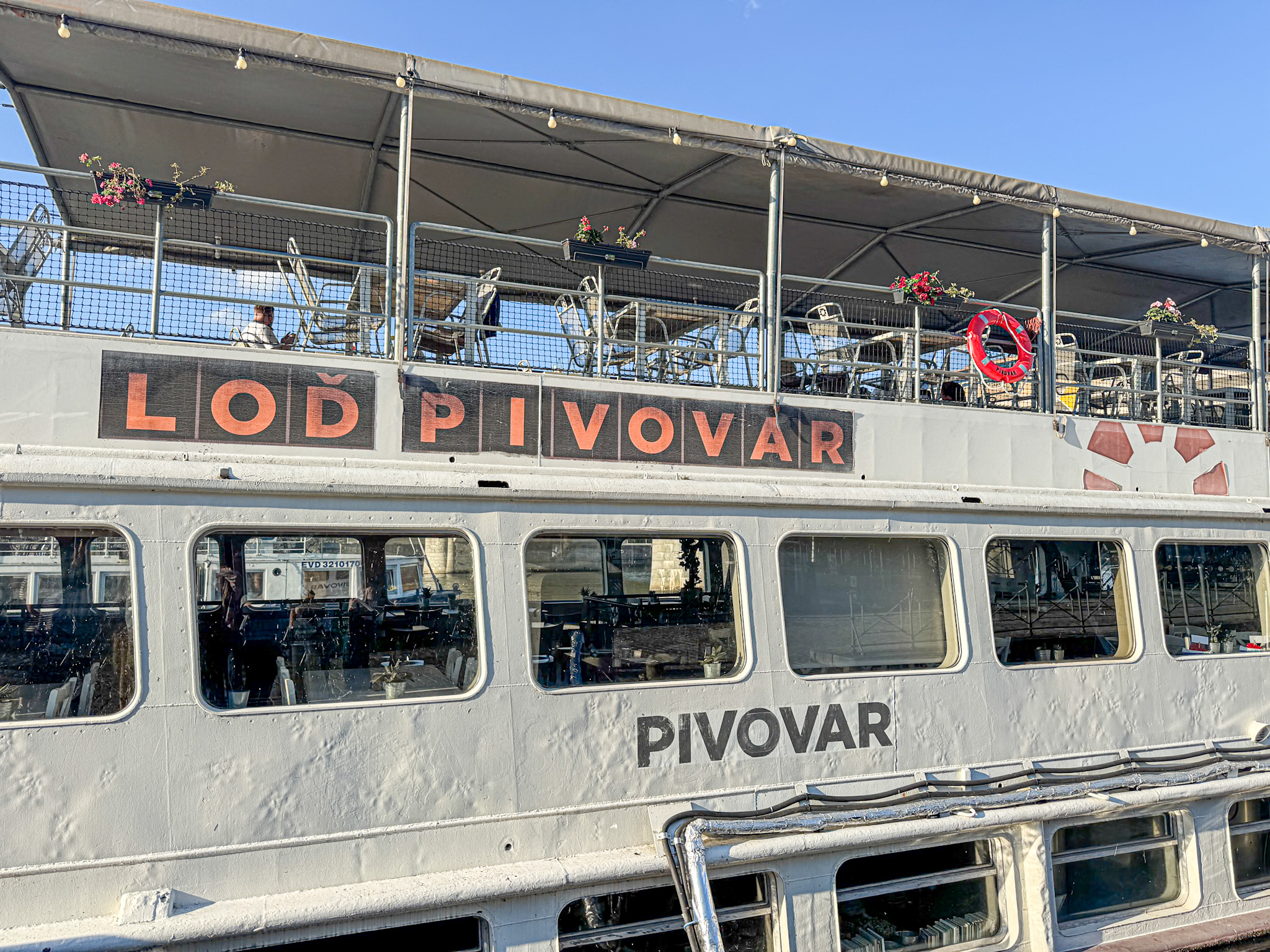 A boat named Loď Pivovar with an upper deck seating area decorated with flowers.