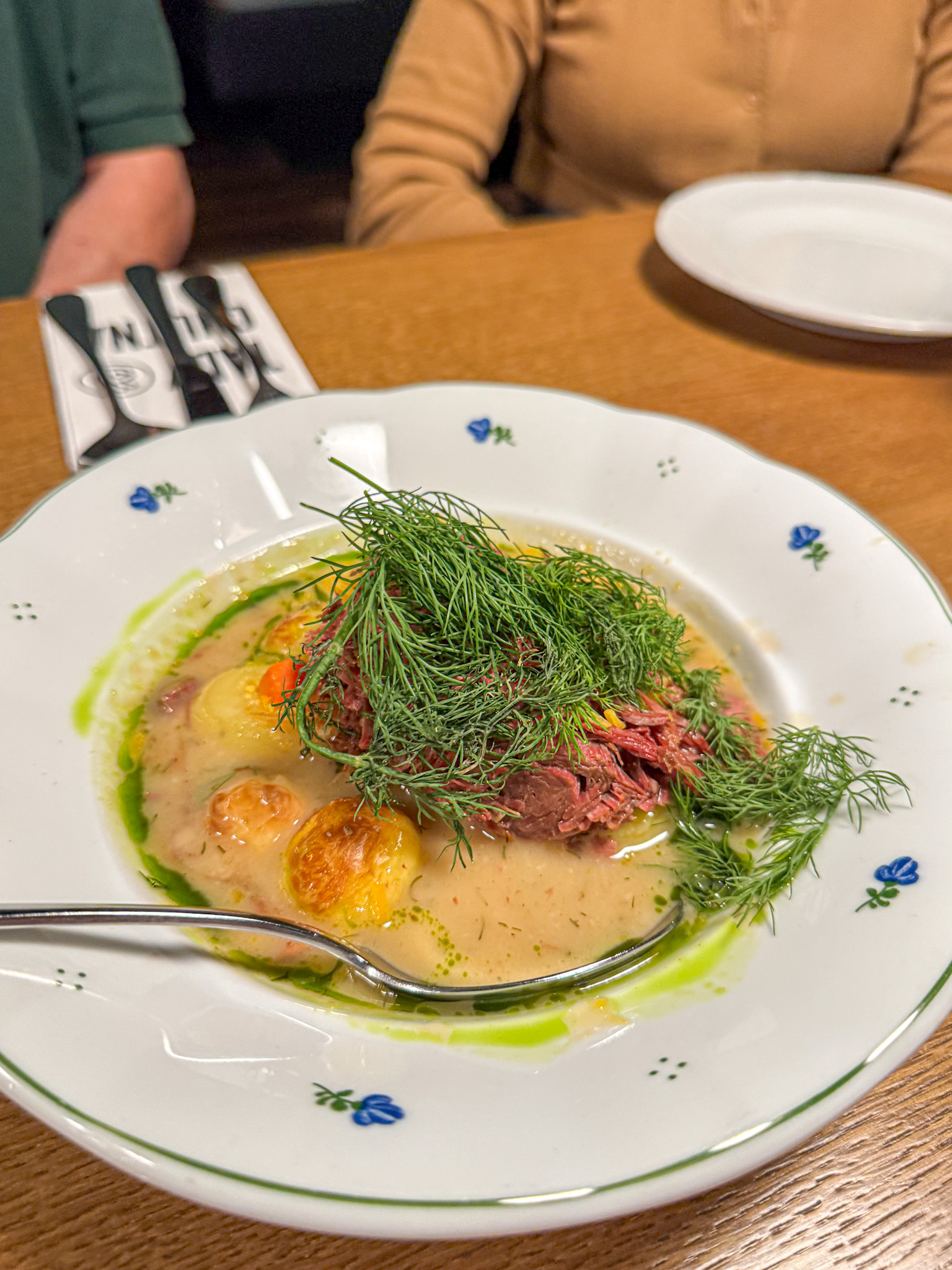A plate of stew with shredded meat, potatoes, carrots, and fresh dill garnish on a wooden table in Prague.