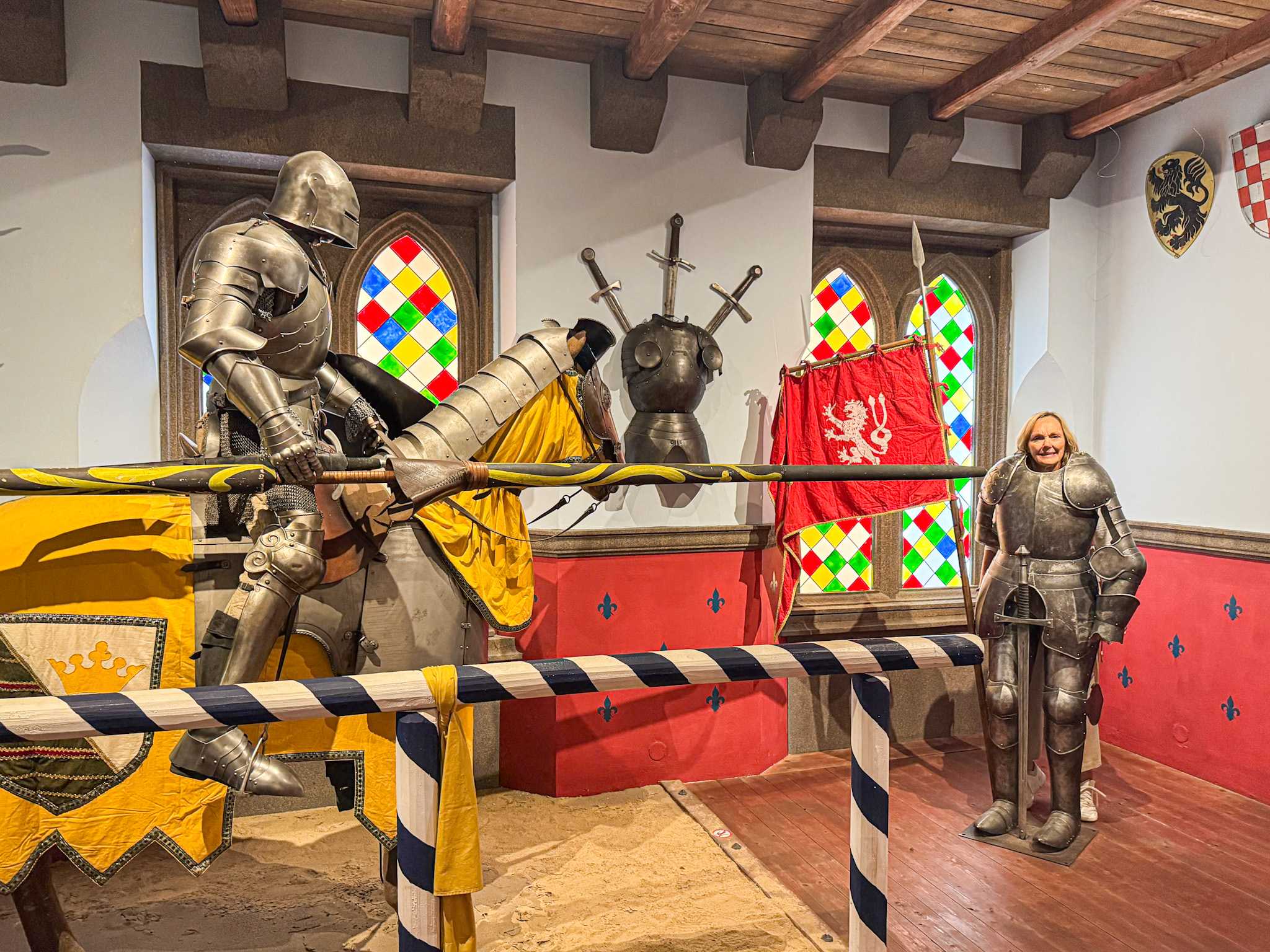 Exhibit with knight mannequins jousting and a smiling person in armor, with colorful stained glass windows.