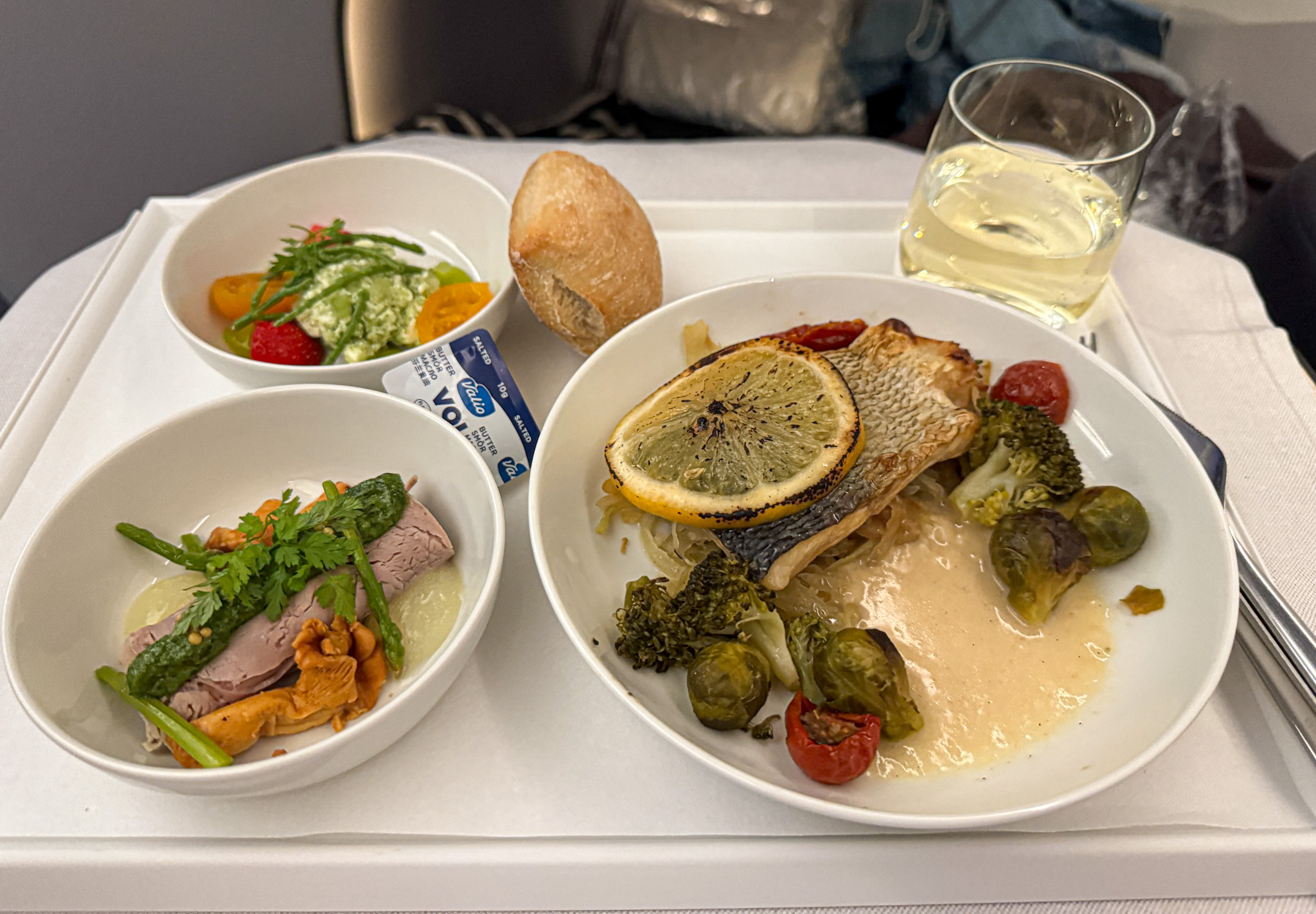 Finnair Business airline meal with fish, vegetables, salad, bread roll, dessert, and a glass of white wine on a tray.