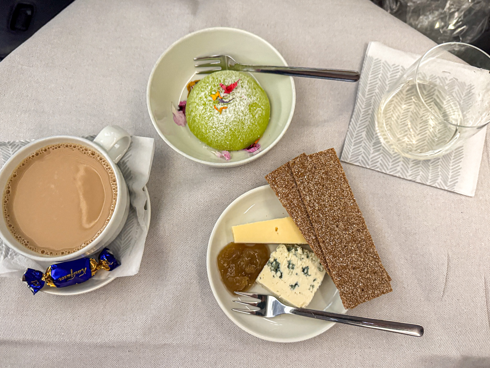 A cup of coffee, a glass of water, cheese, crispbread, fig jam, and a green dessert on a white tablecloth on a Finnair Business class flight.