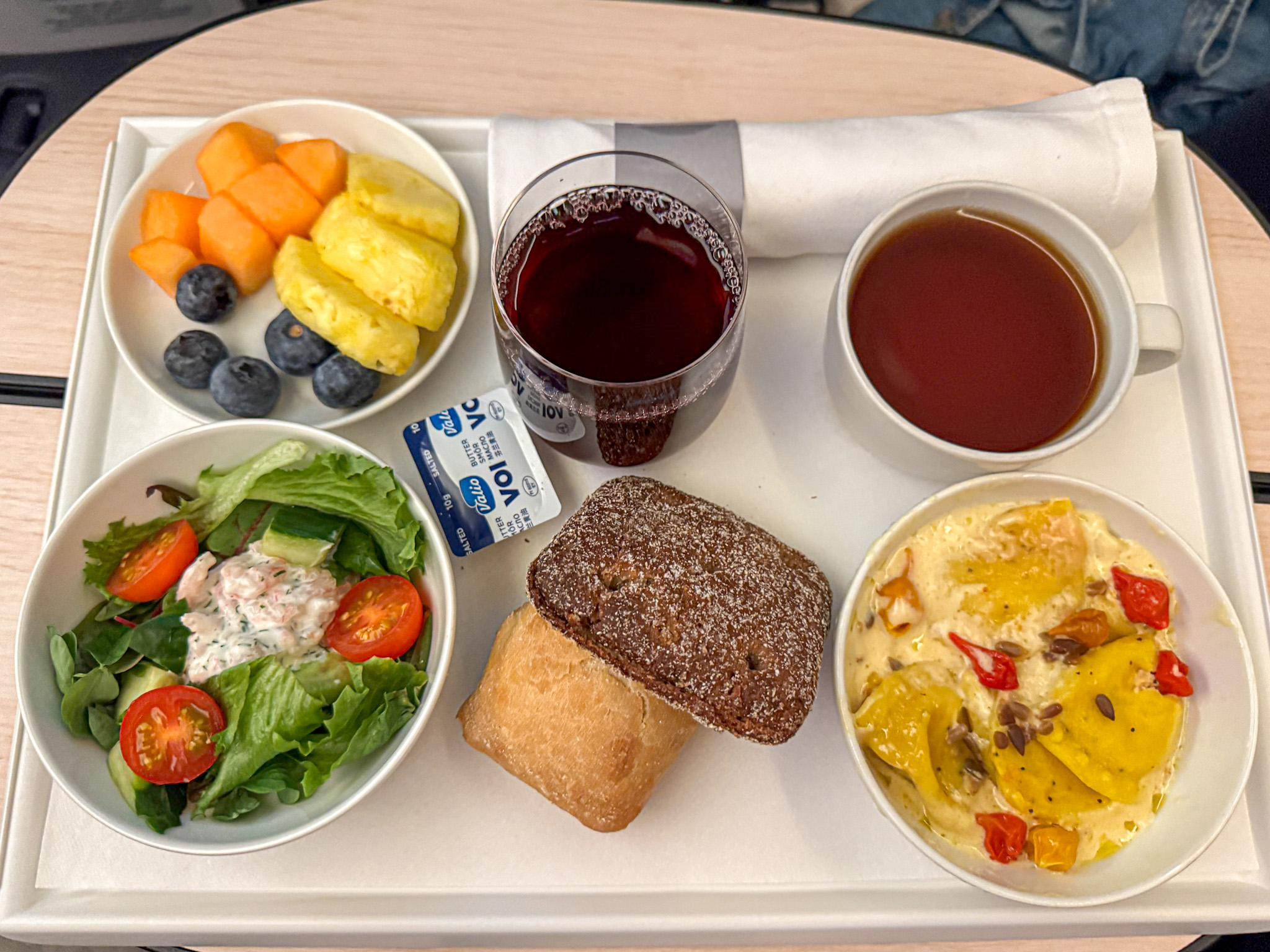 Finnair airplane meal tray with fruit, salad, bread rolls, a cup of tea, red wine, and a ravioli dish.
