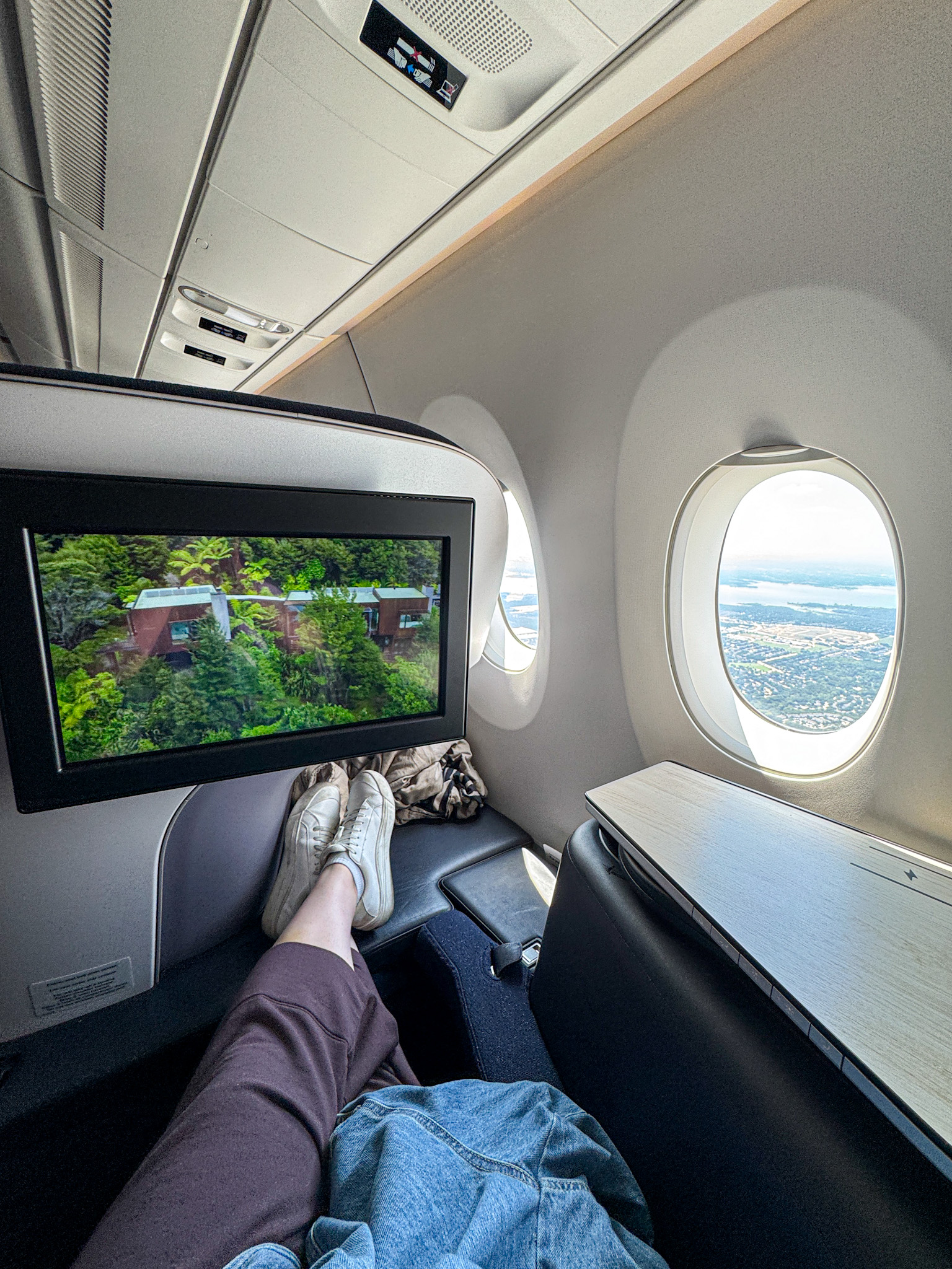 Person relaxing in a Finnair business class airplane seat with feet up, watching TV, and looking out the window at the landscape below.