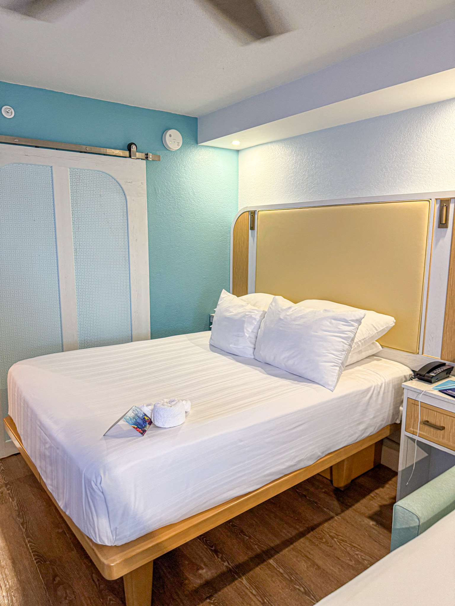 A neatly made hotel bed with two pillows, a towel, and a pamphlet in a bright, modern room at Caribbean Beach hotel at Disney.