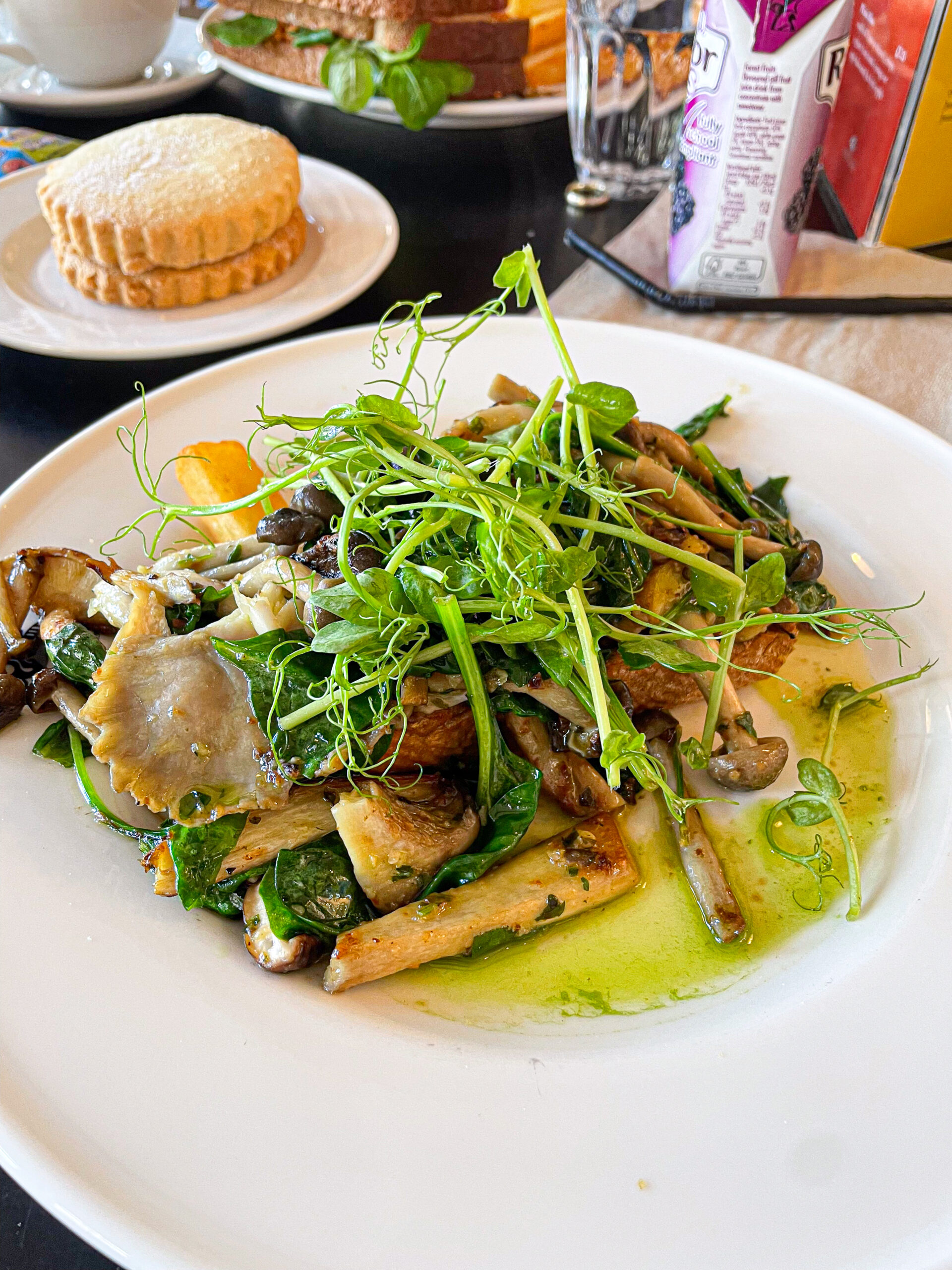 A plate of sautéed mushrooms and greens garnished with fresh pea shoots, with biscuits in the background.