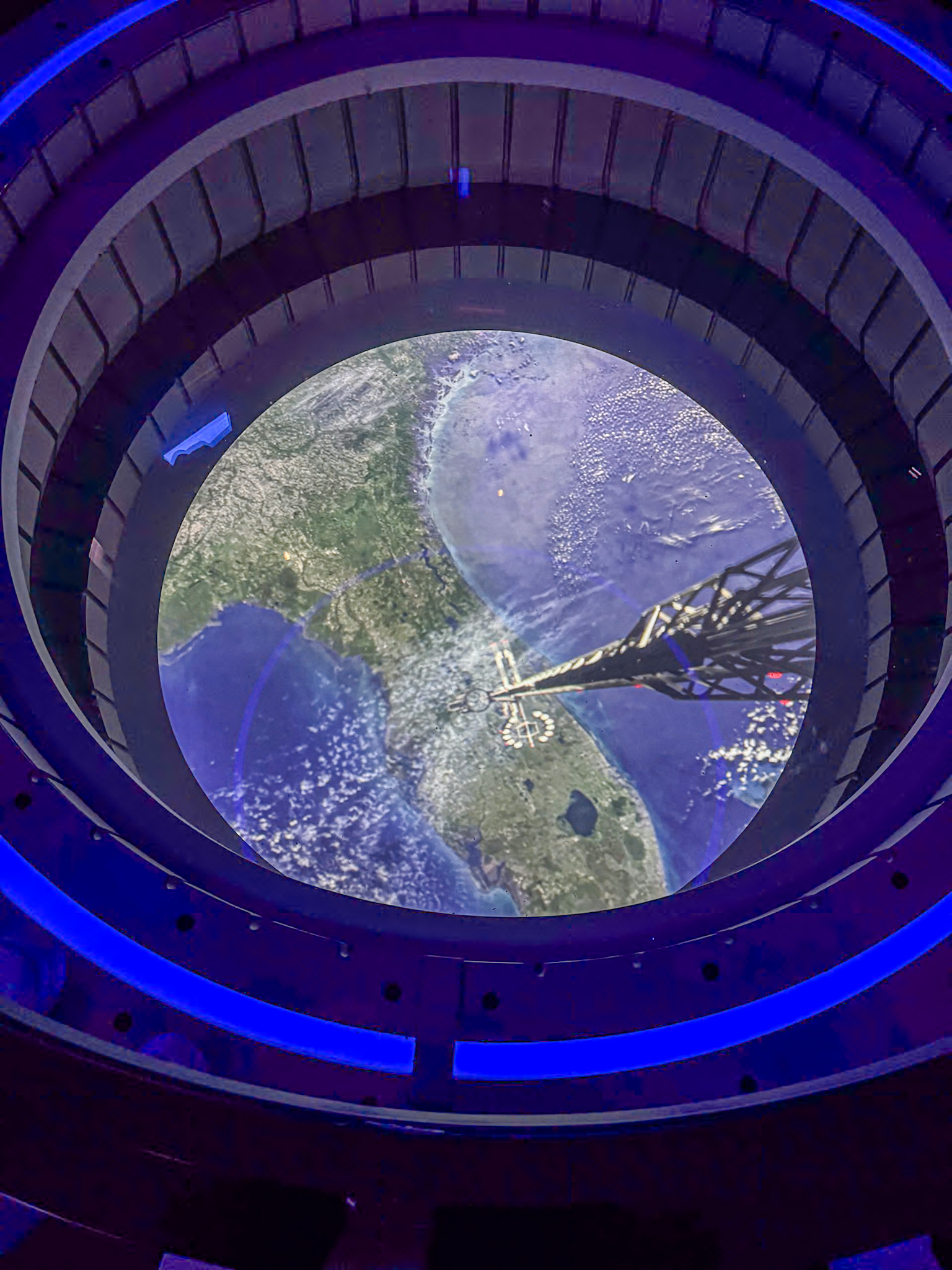 Circular window view of Florida from space with spacecraft shadow and glowing blue lights around the frame on Disney's Space Elevator.