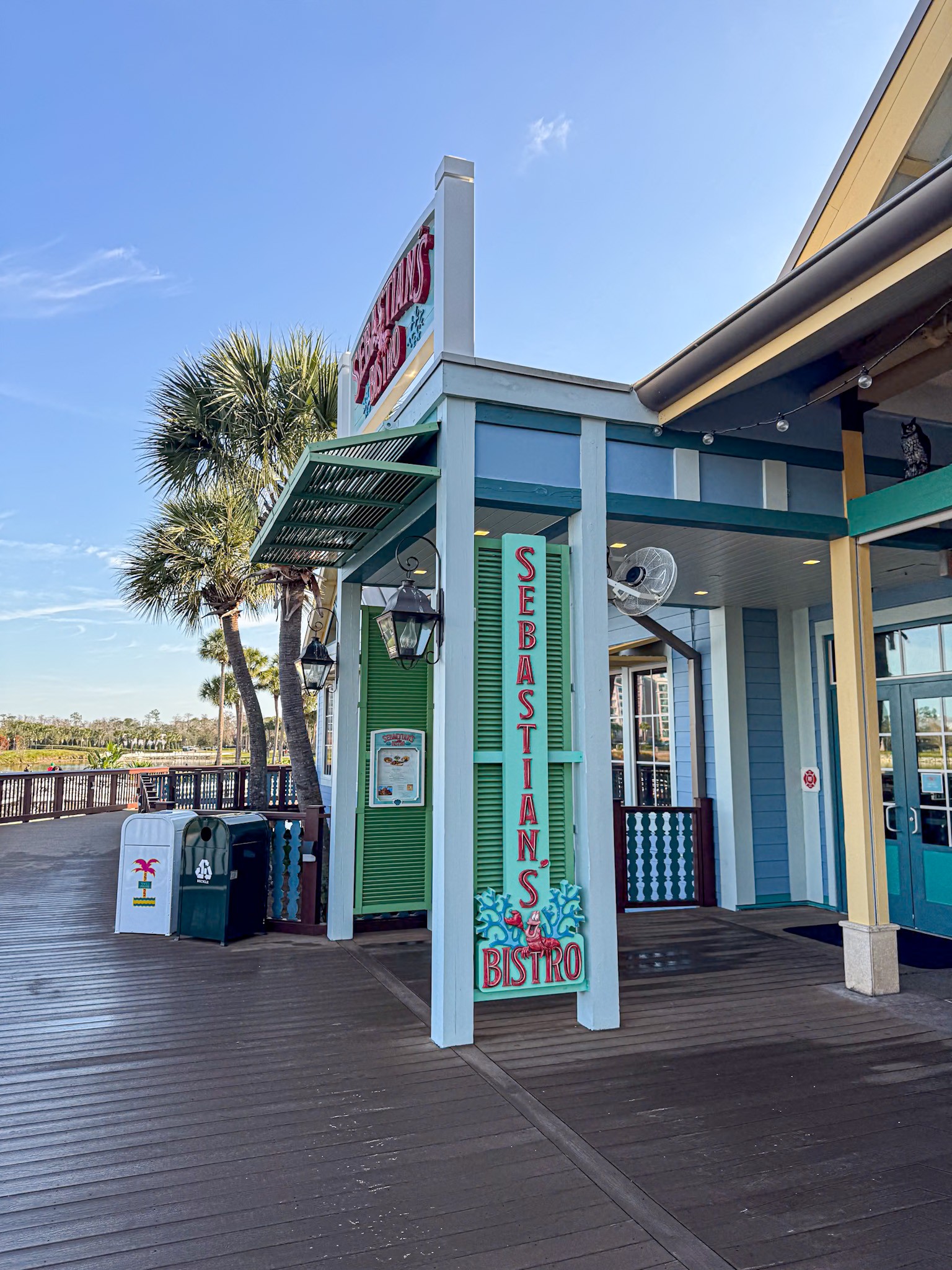 Exterior of Sebastians Bistro with colorful sign, palm trees, and boardwalk under a clear sky.