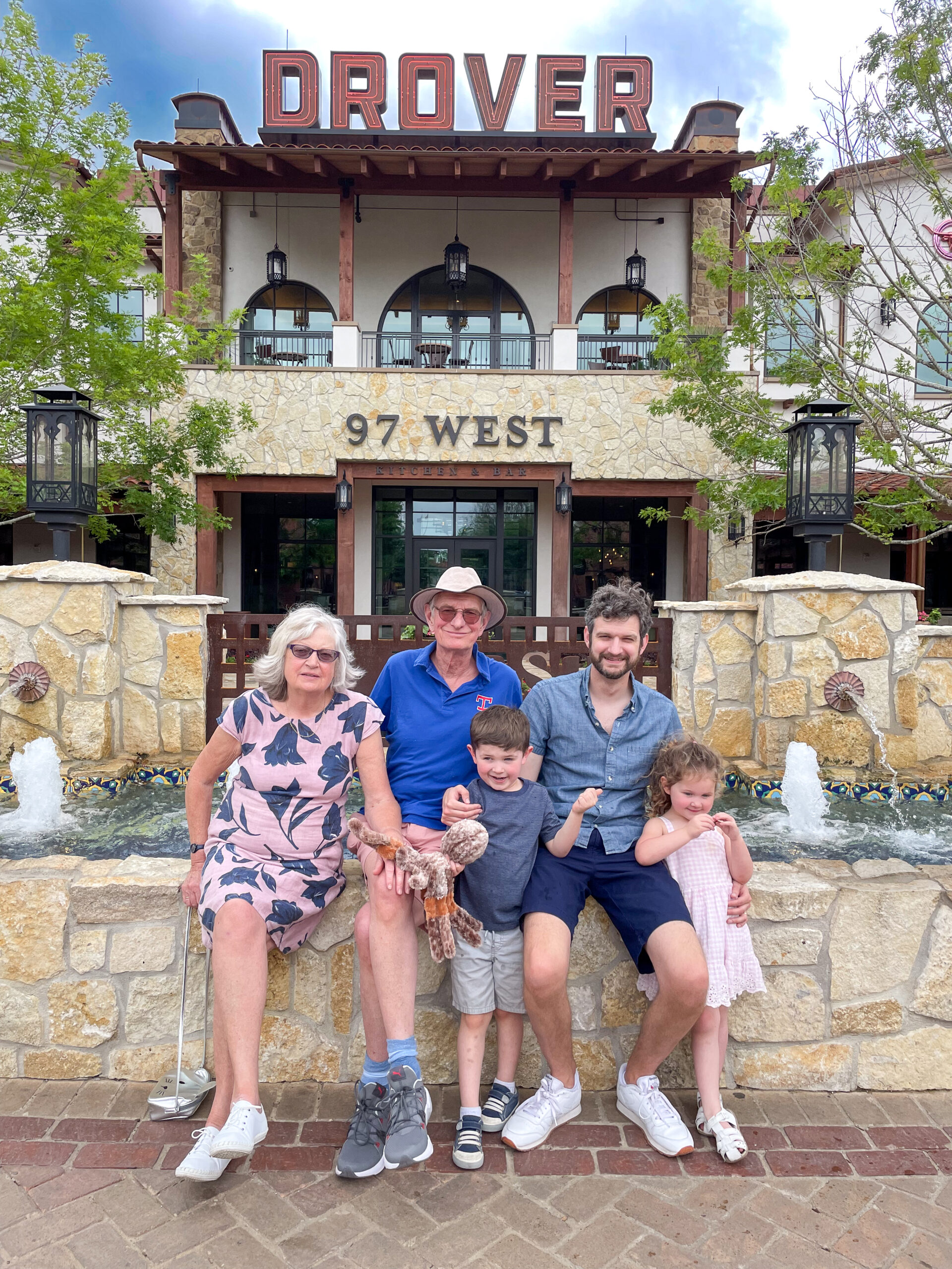 A family of five poses and smiles in front of Hotel Drover, sitting by a fountain at 97 West.