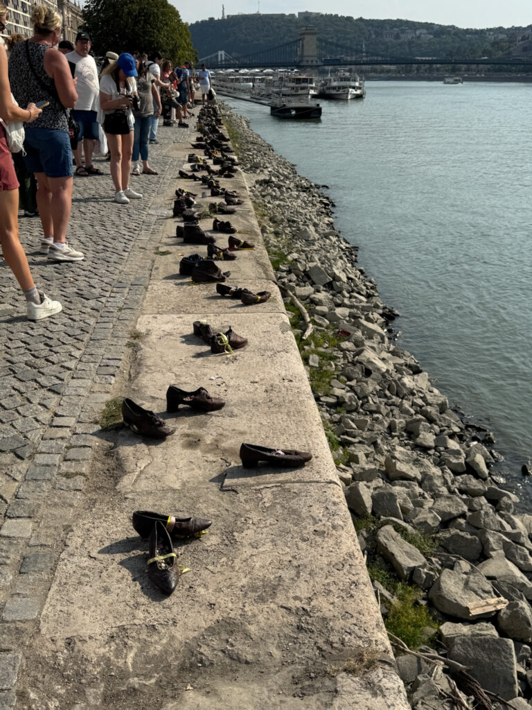 People stand by the Danube River next to bronze shoes from the Holocaust memorial in Budapest.