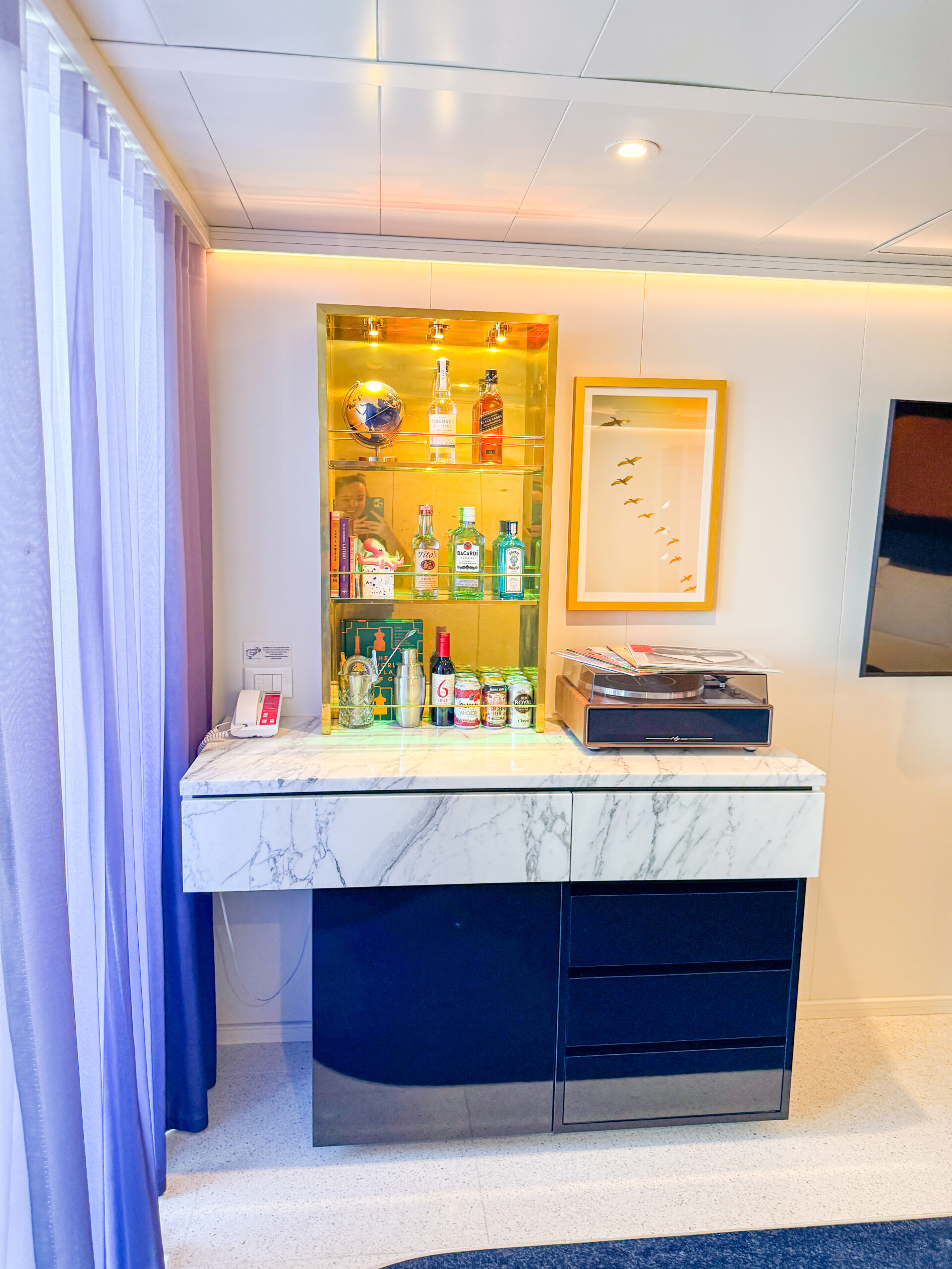 A marble-topped bar with liquor bottles, glasses, and a record player in a modern, brightly lit room.