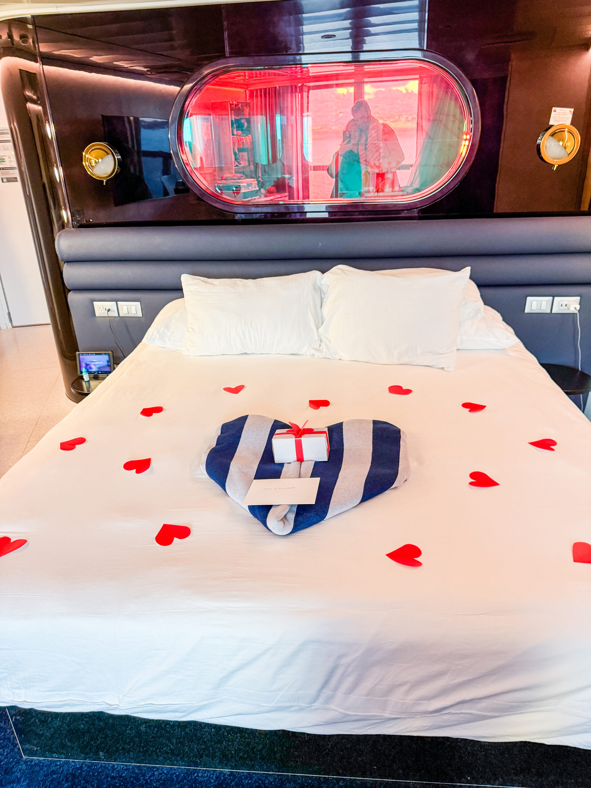 A bed decorated with red heart shapes, a towel folded into a heart, and a gift box on top.